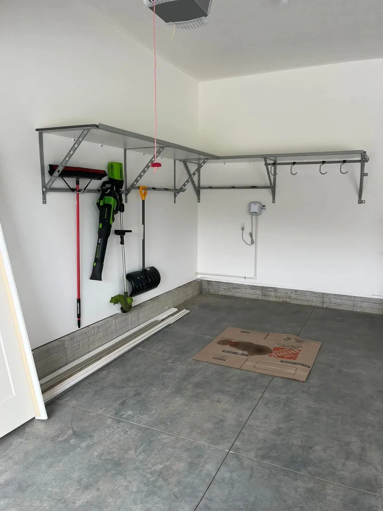 A sparse garage corner highlighting common garage layout mistakes, featuring a basic wall-mounted rail system that lacks the flexibility of slatwalls or cabinets, leading to floor clutter and exposed concrete stains.
